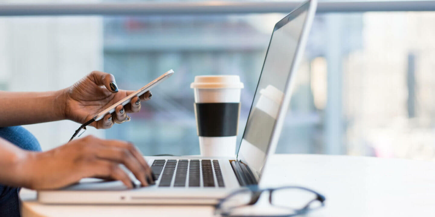 Hands on laptop with mobile and coffee cup